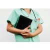 Woman wearing green nursing scrubs with a stethoscope around her neck while holding a laptop