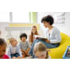 Woman sitting on a bean bag and reading from a book, while her young students are listening