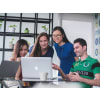 Students gathered around a table looking at the same laptop screen