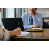 Woman signing a document while a male is sitting across her