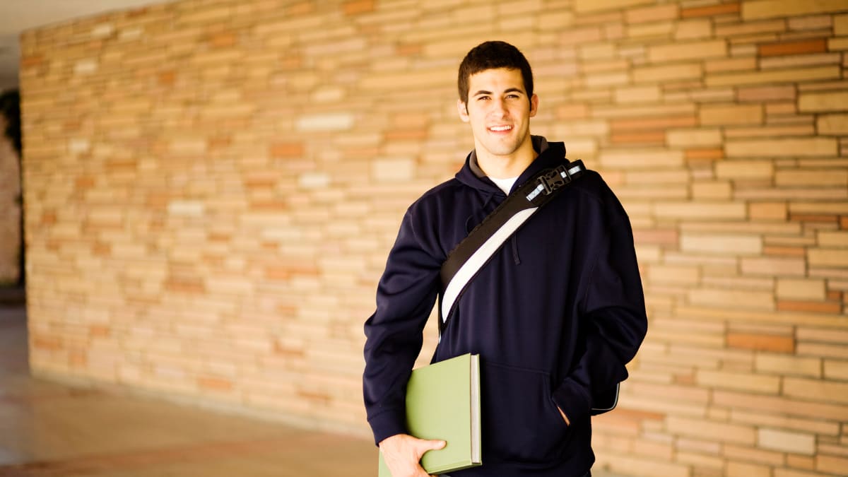 Male student smiling with a green book