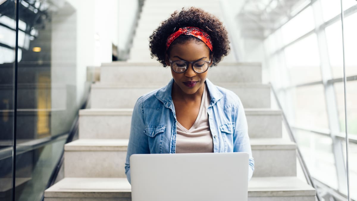 Female student on a laptop at the bottom of stairs