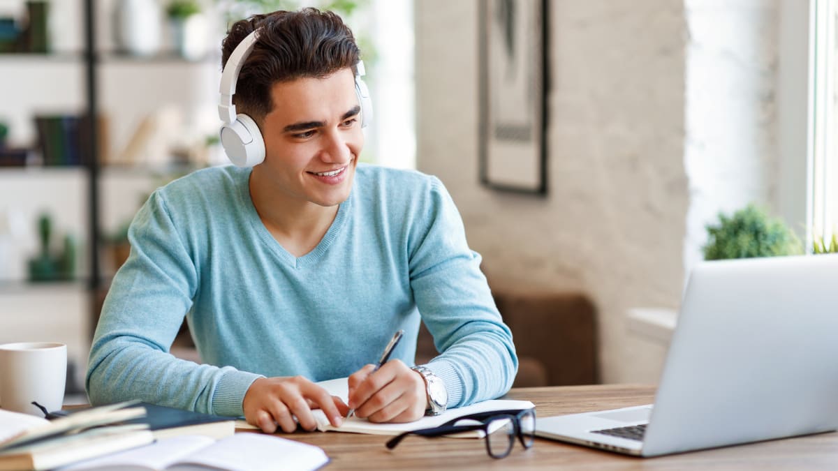 Man writing in a notebook and staring at a laptop