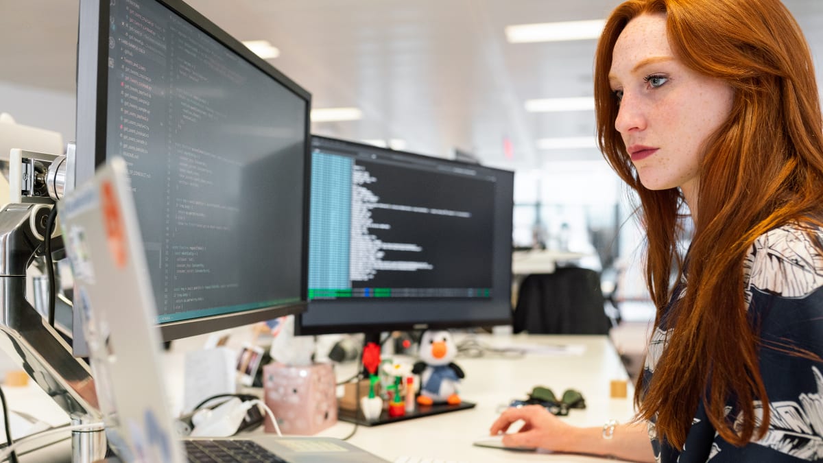 Woman coding on three computers