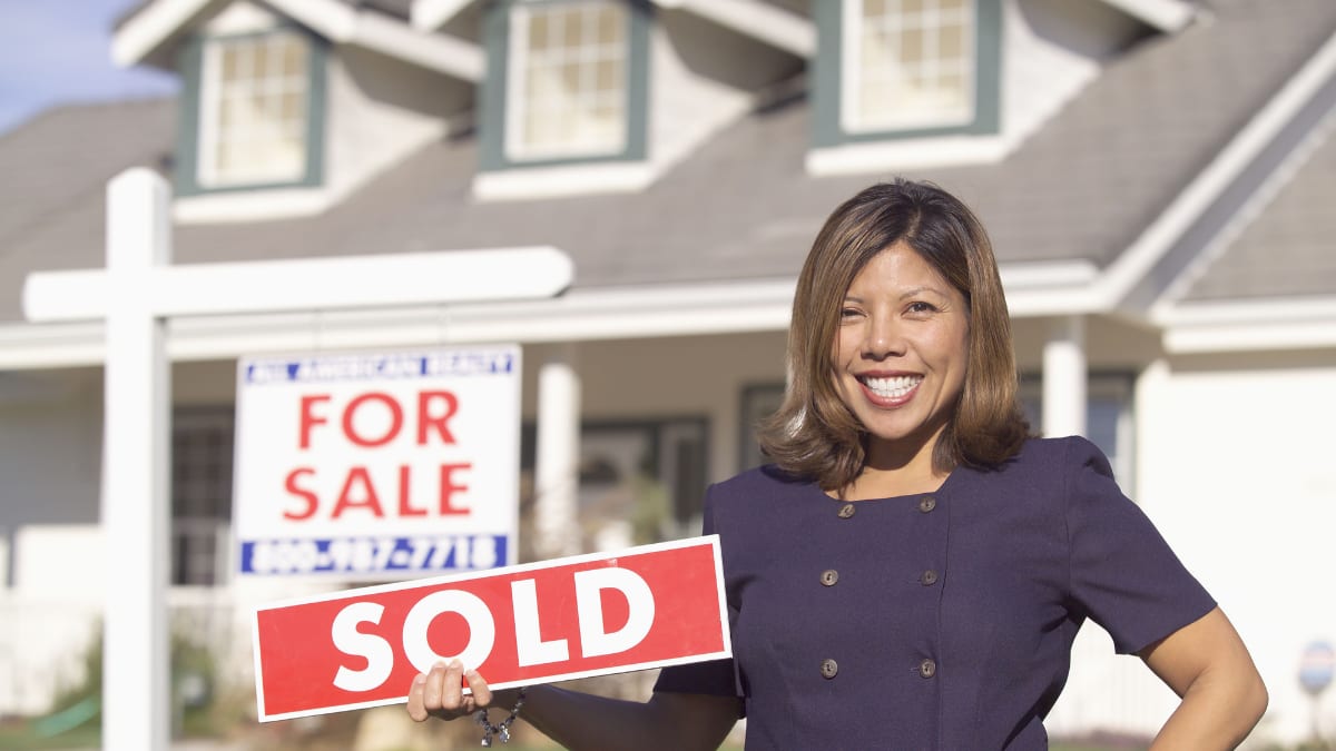 Real estate agent holding a sold sign in front of a house