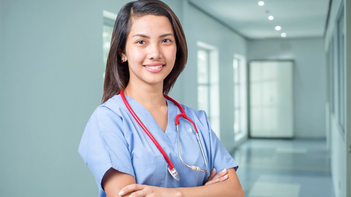 Female nurse smiling with arms crossed in a hallway