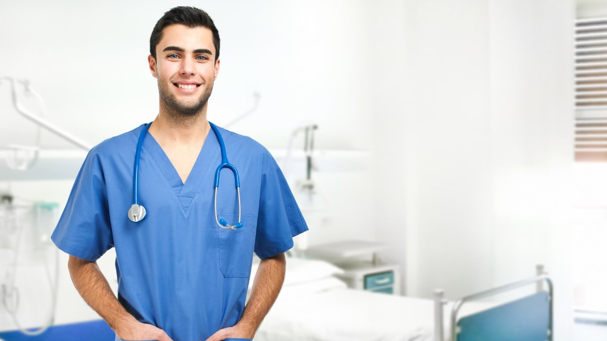 Smiling male nurse standing next to a hospital bed