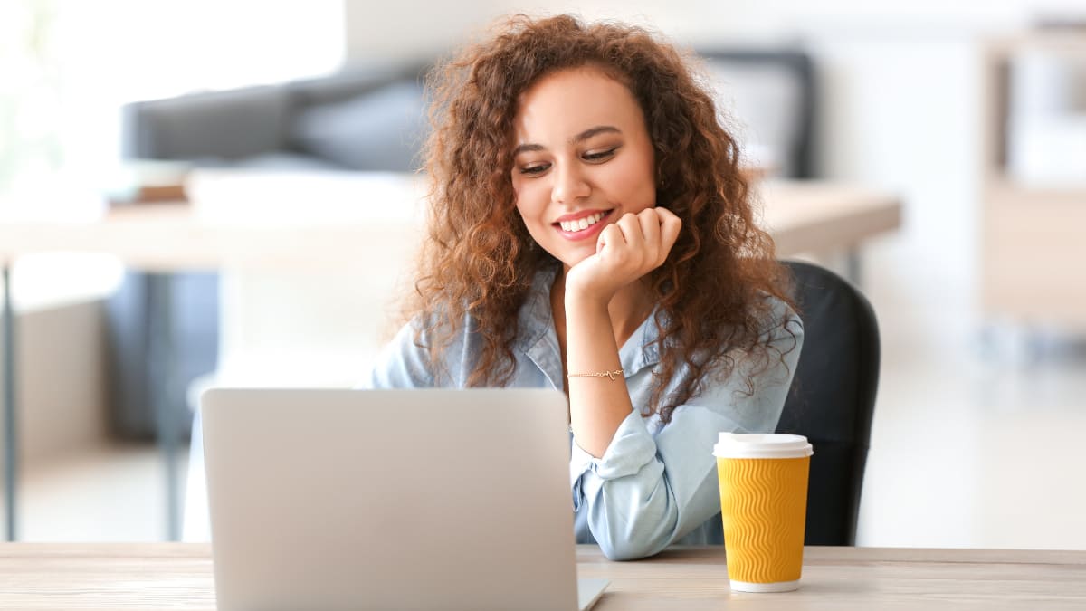 Female student smiling at laptop with cup of coffee