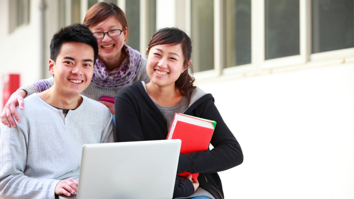 Group of students smiling on laptop outside