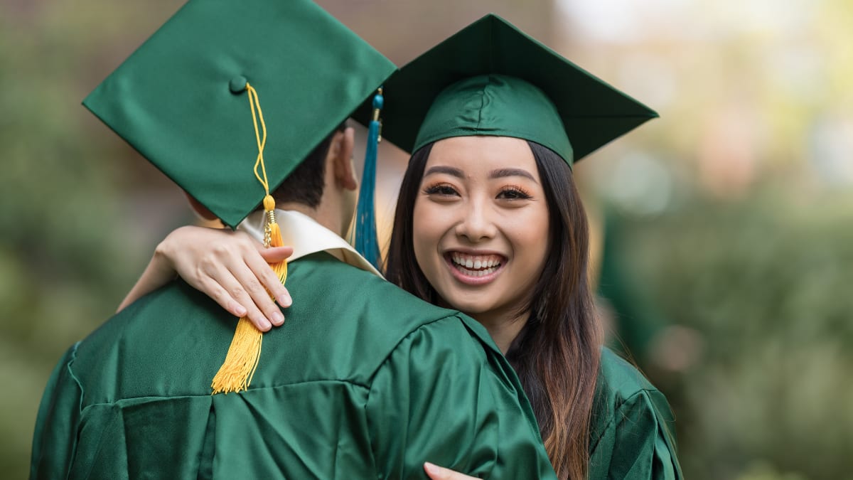 Two happy graduates in green cap and gown