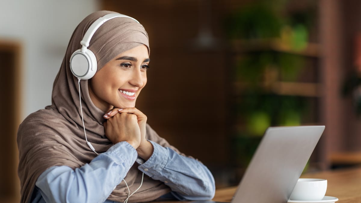 Woman smiling at a laptop with headphones