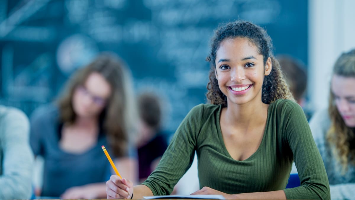 Student smiling in a classroom with a pencil in hand