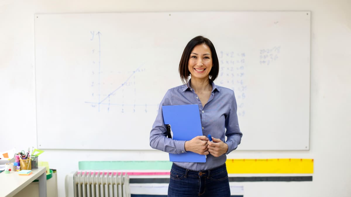Female teacher standing with notebook in front of a whiteboard