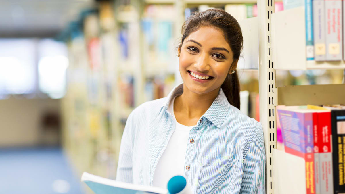 Female student smiling with a book in the library