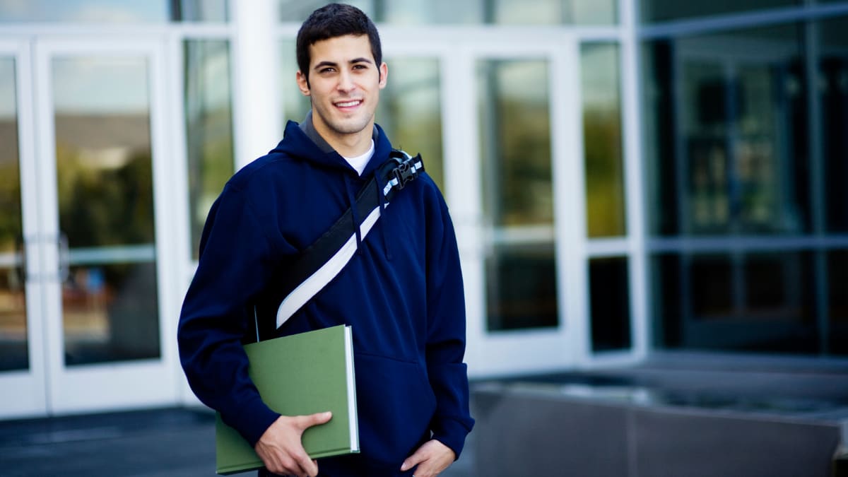 Male student in a blue hoodie holding notebooks