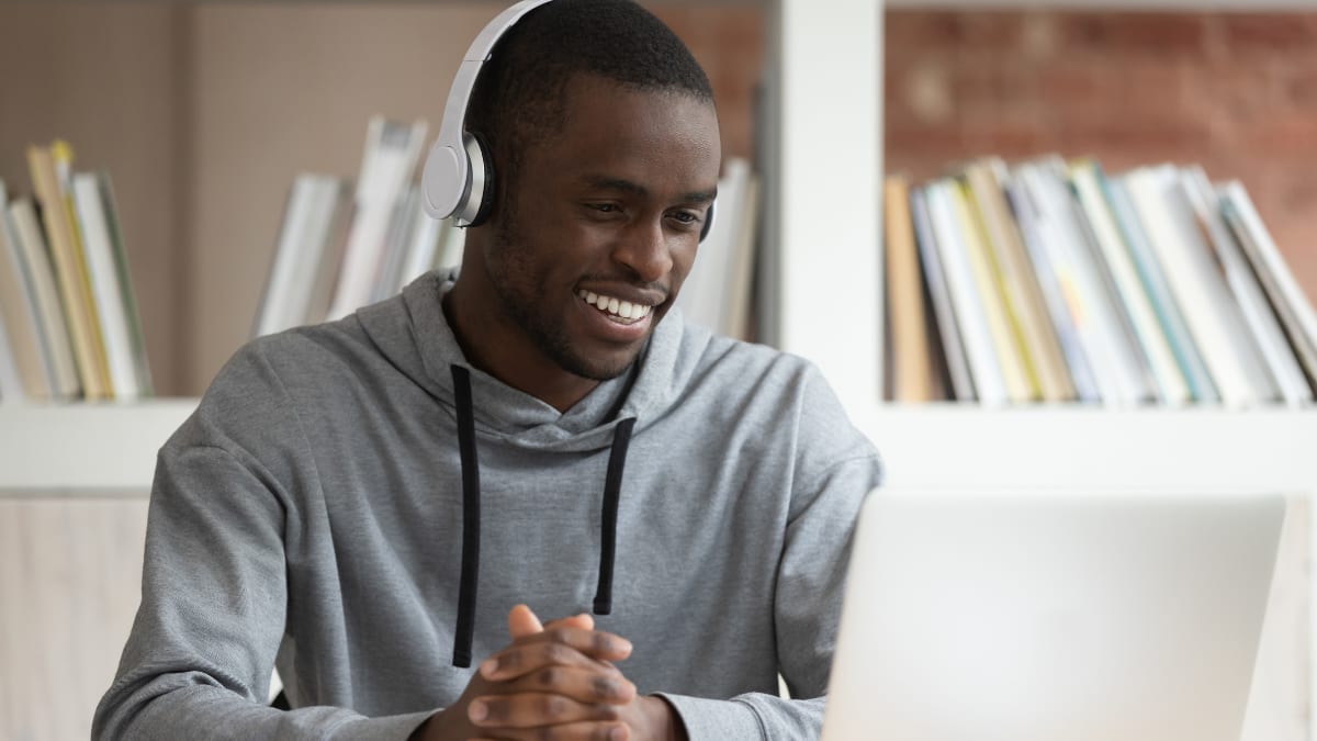 Male student with headphones smiling at a laptop