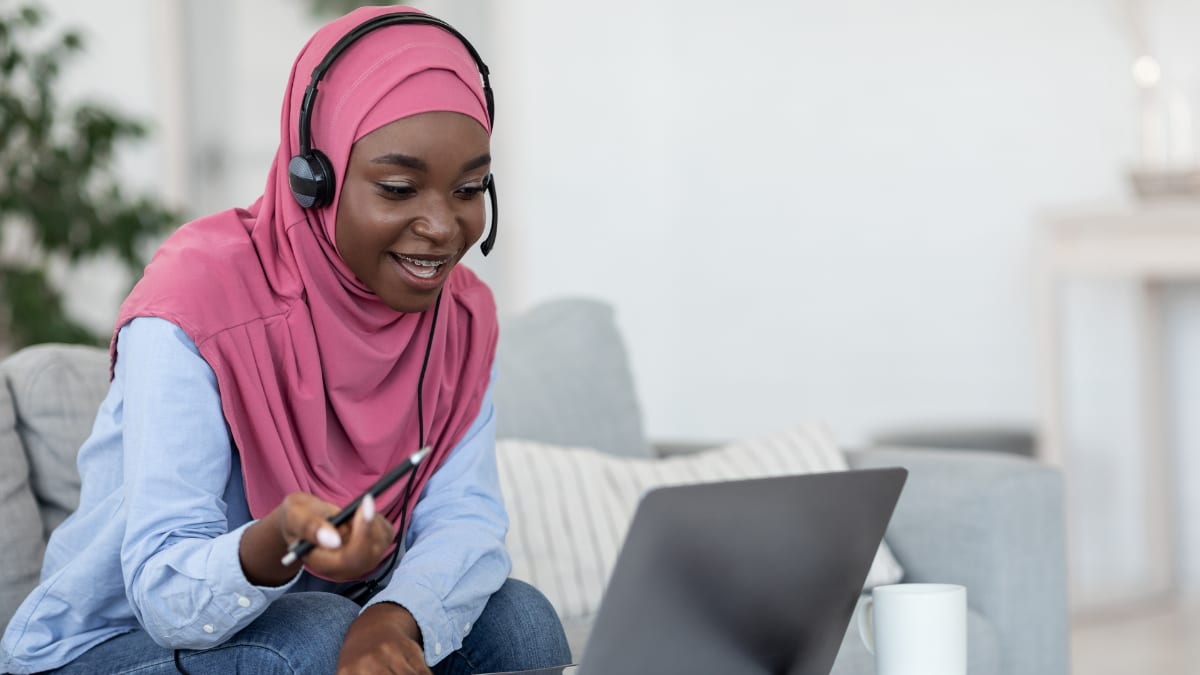 Female student with a pen smiling at a laptop