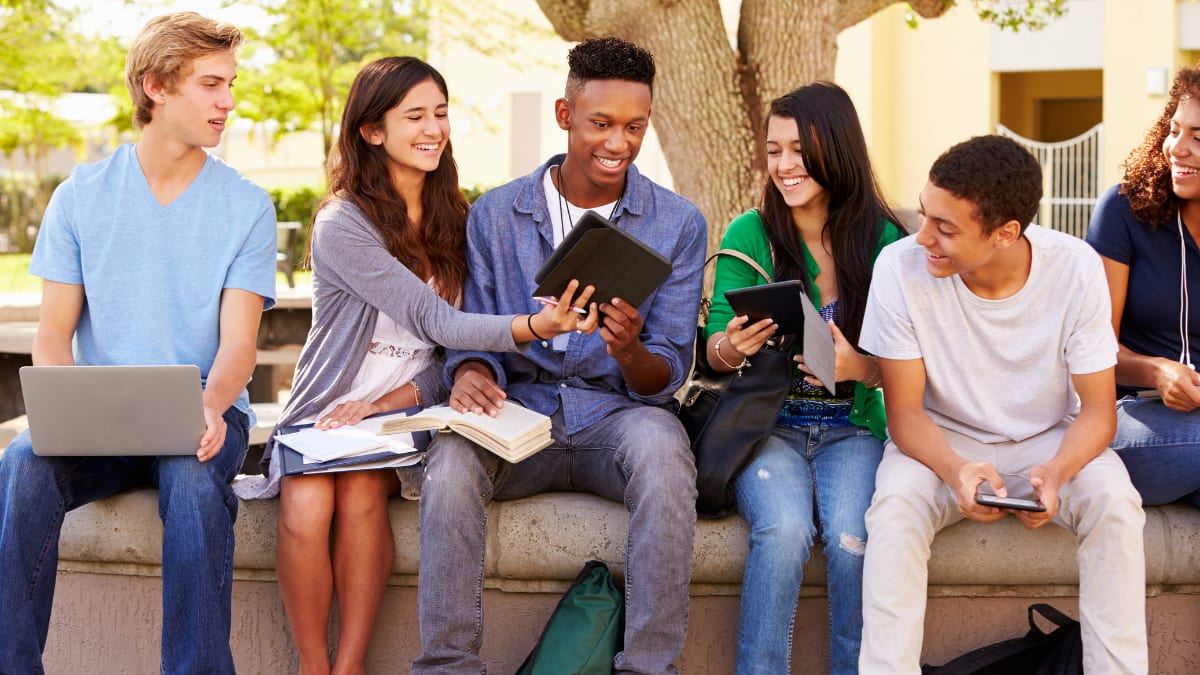 Students looking at an electronic tablet next to a tree