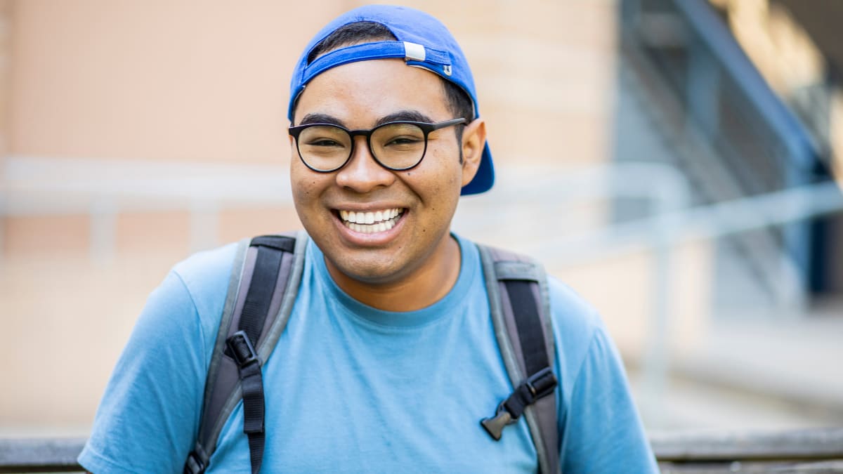 Man smiling with a backwards hat, glasses and a backpack