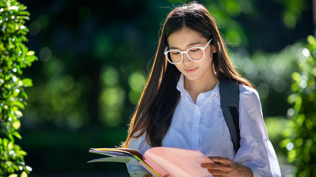 Female student with white glasses studying a notebook outside