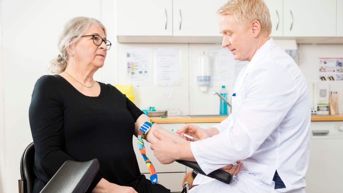 Male phlebotomist helping an older woman