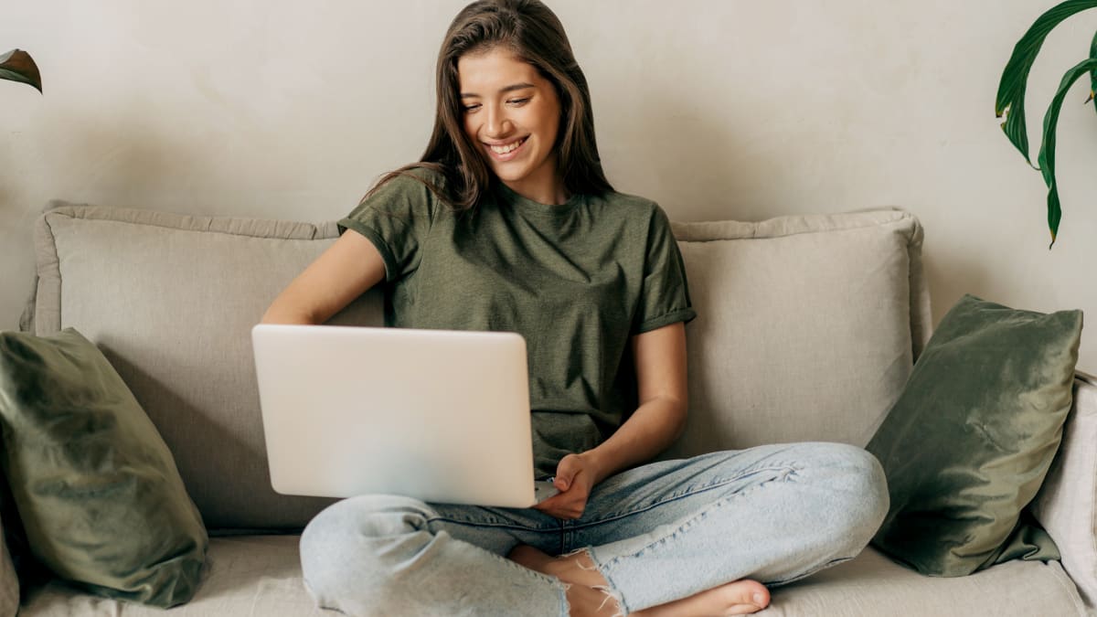 Woman smiling at her laptop on a sofa
