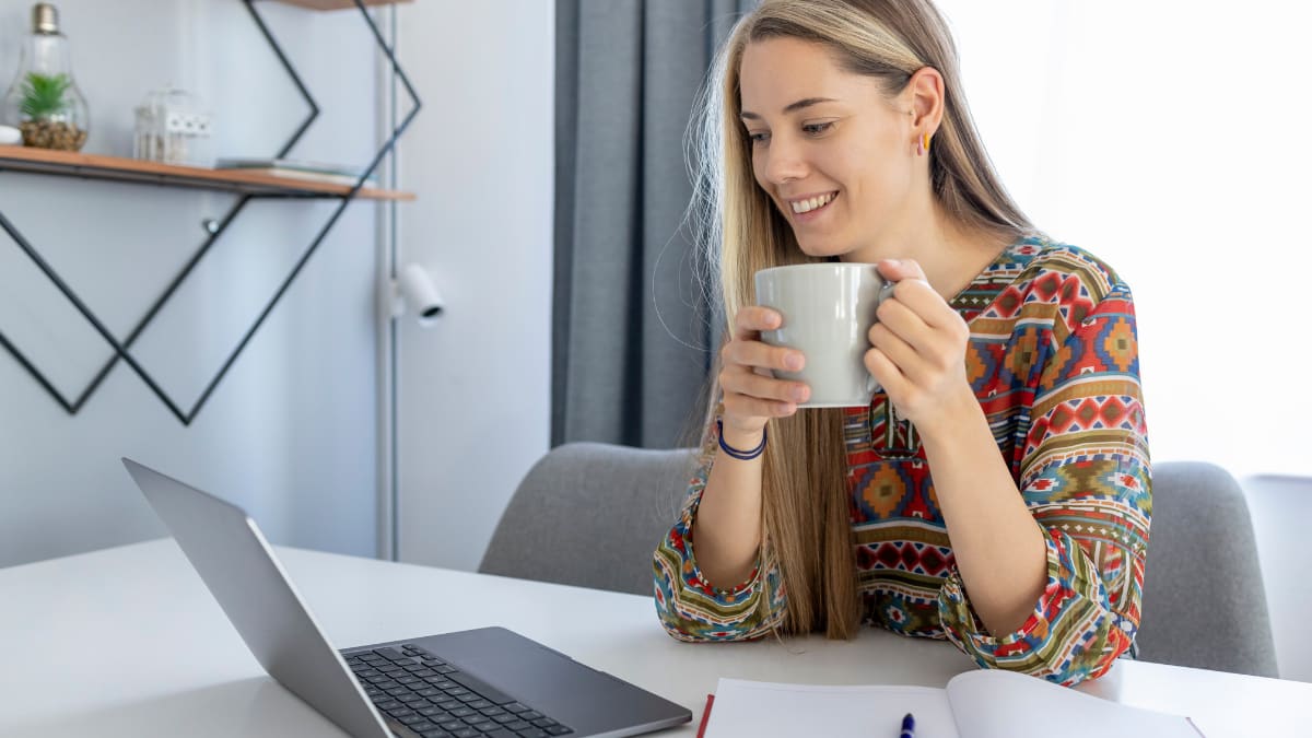 Female public relations student holding a cup of coffee next to laptop