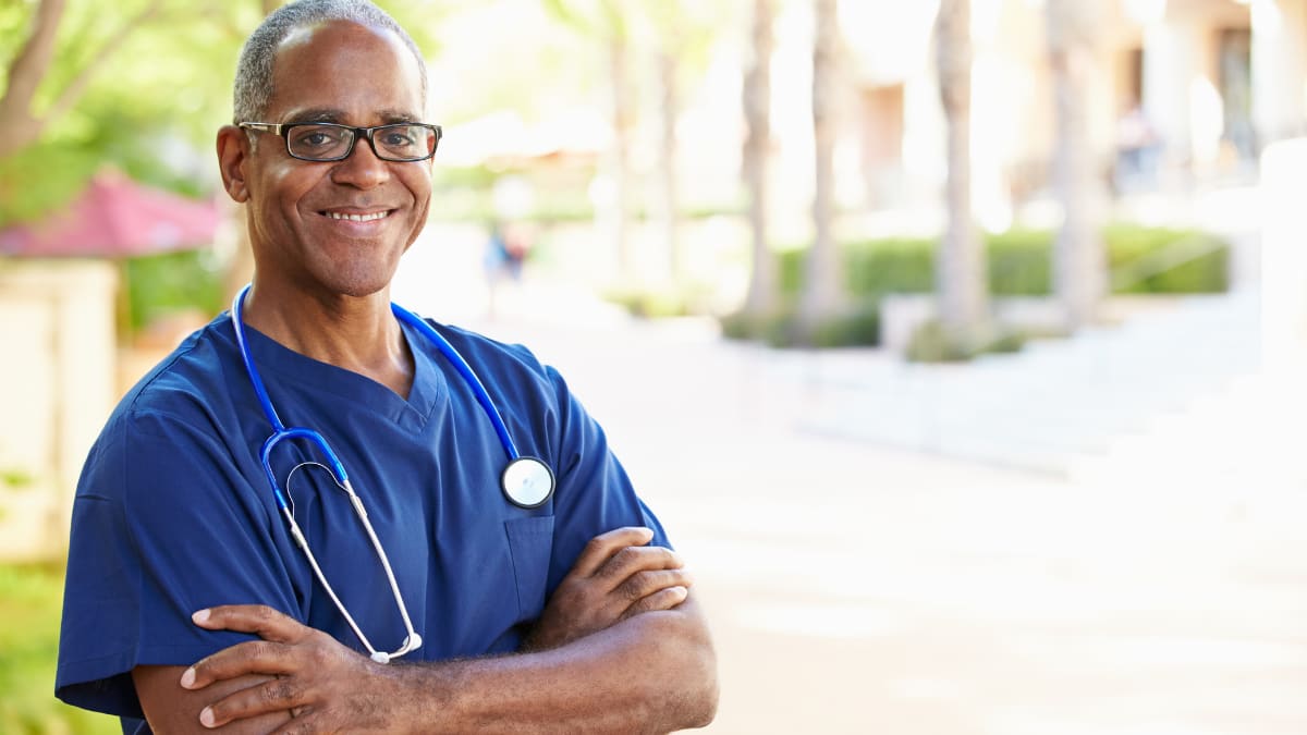 Male nurse smiling outside with arms folded