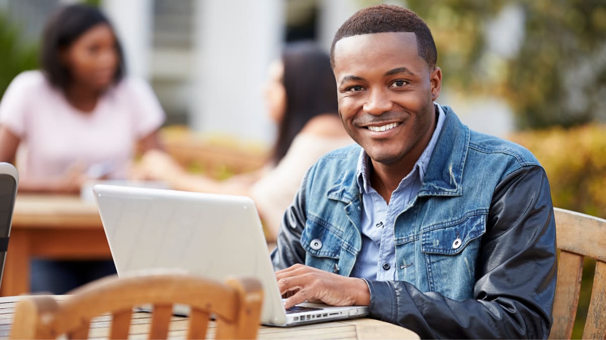 Man smiling at table outside with laptop