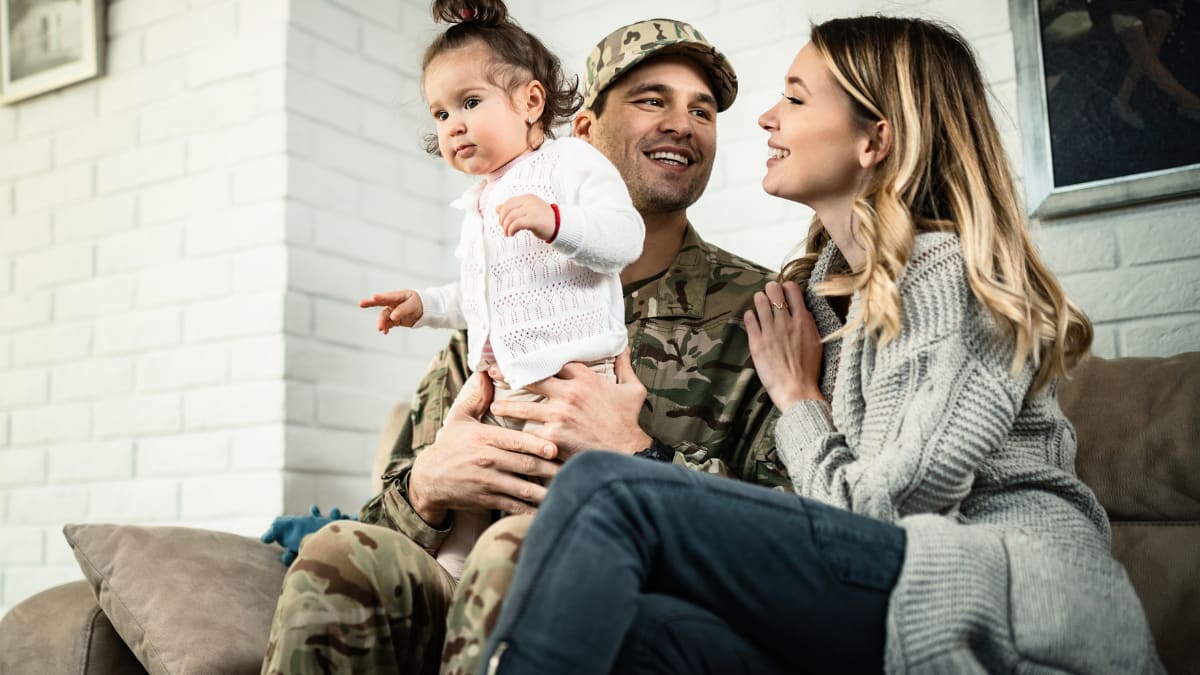 Man in military uniform smiling with wife and baby