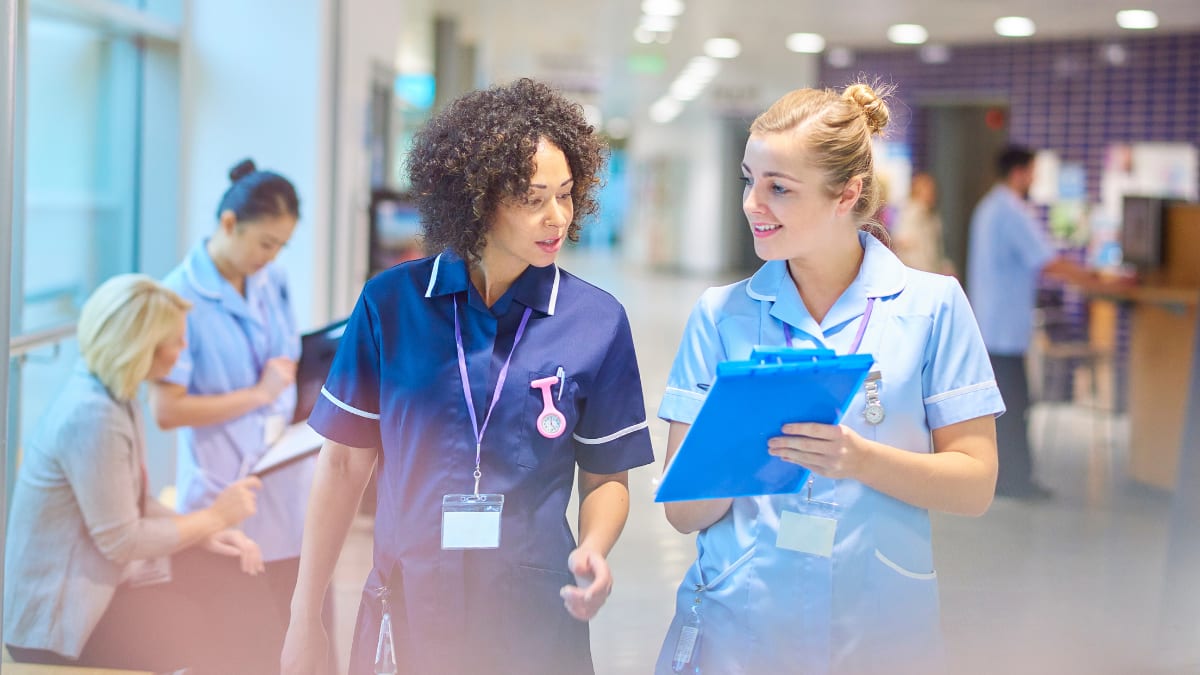 Two female nurses walking together and discussing a patient's chart