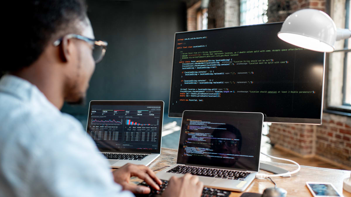 Young computer programmer writing code in front of three monitors