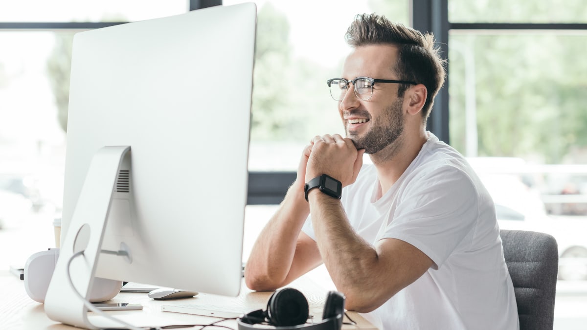 Computer programmer smiling at his desk in front of a large monitor