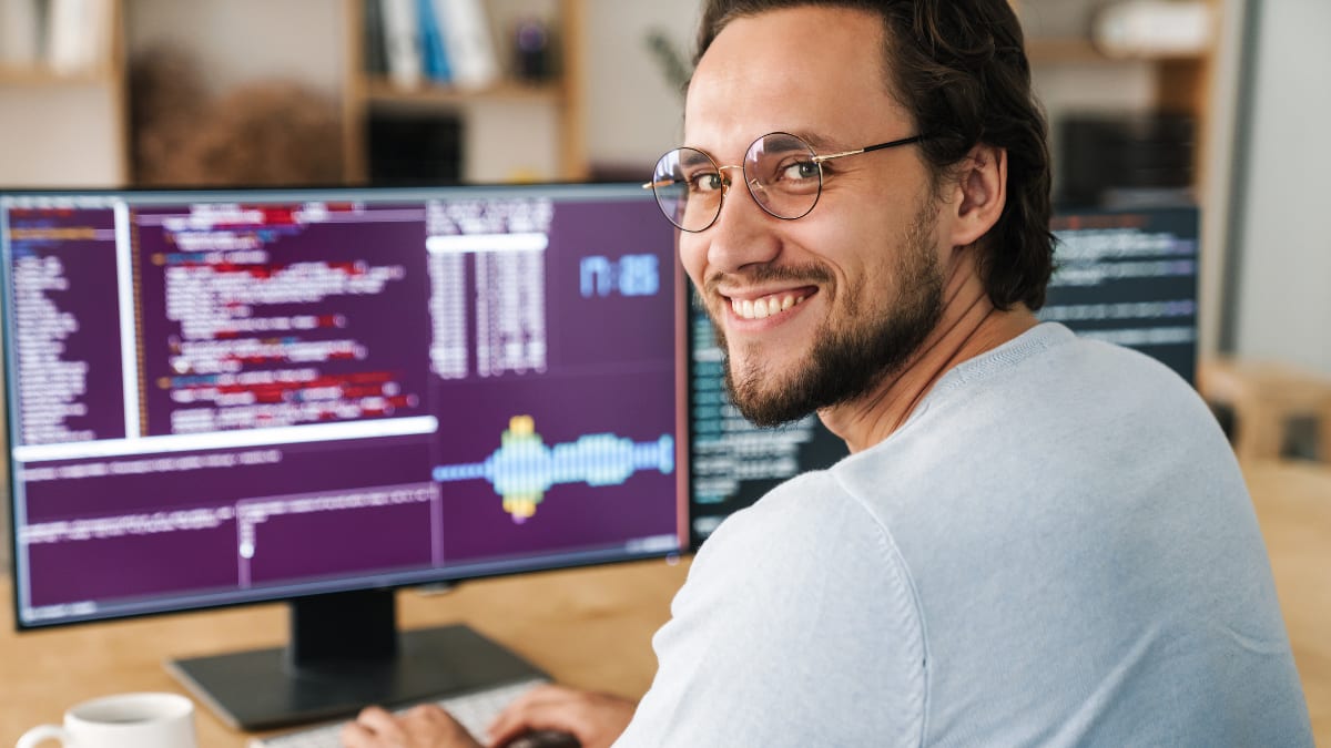 Computer programmer smiling sitting in front of a large computer monitor