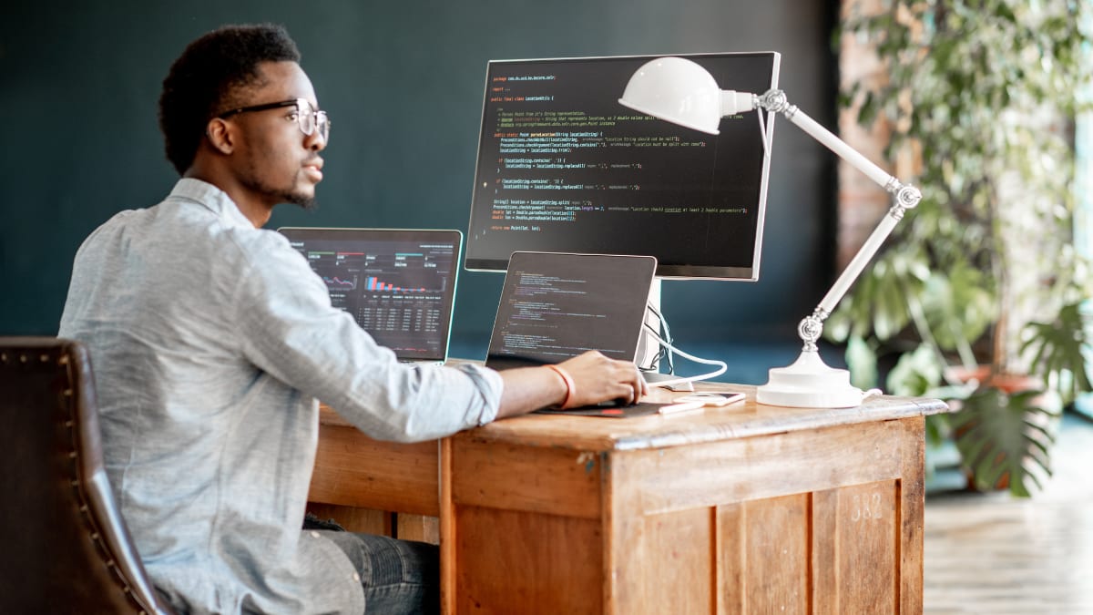 computer programmer sitting at a desk in front of several computer monitors