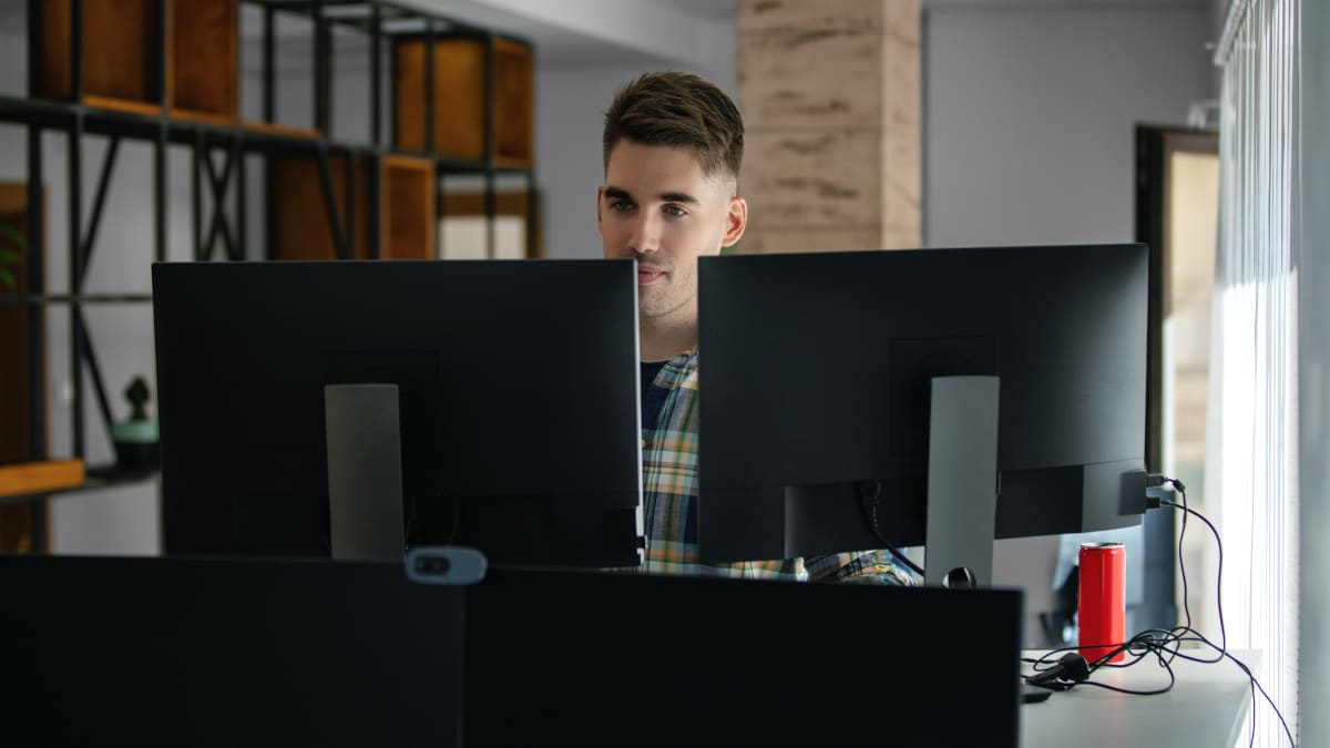 computer programmer sitting at a desk in front of two computer monitors