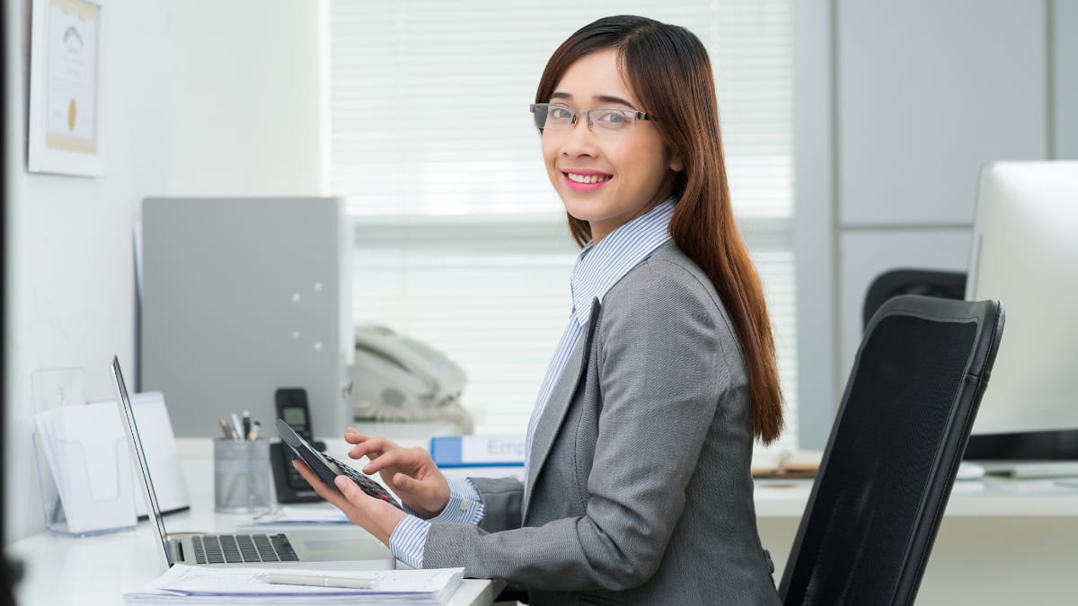 accountant sitting at a desk in front of a computer with a calculator in her hand