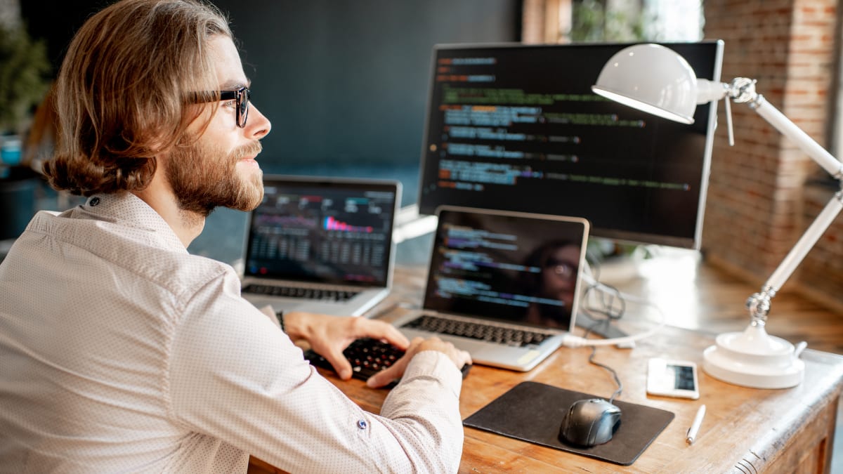 information technology professional sitting at a desk in front of multiple computers