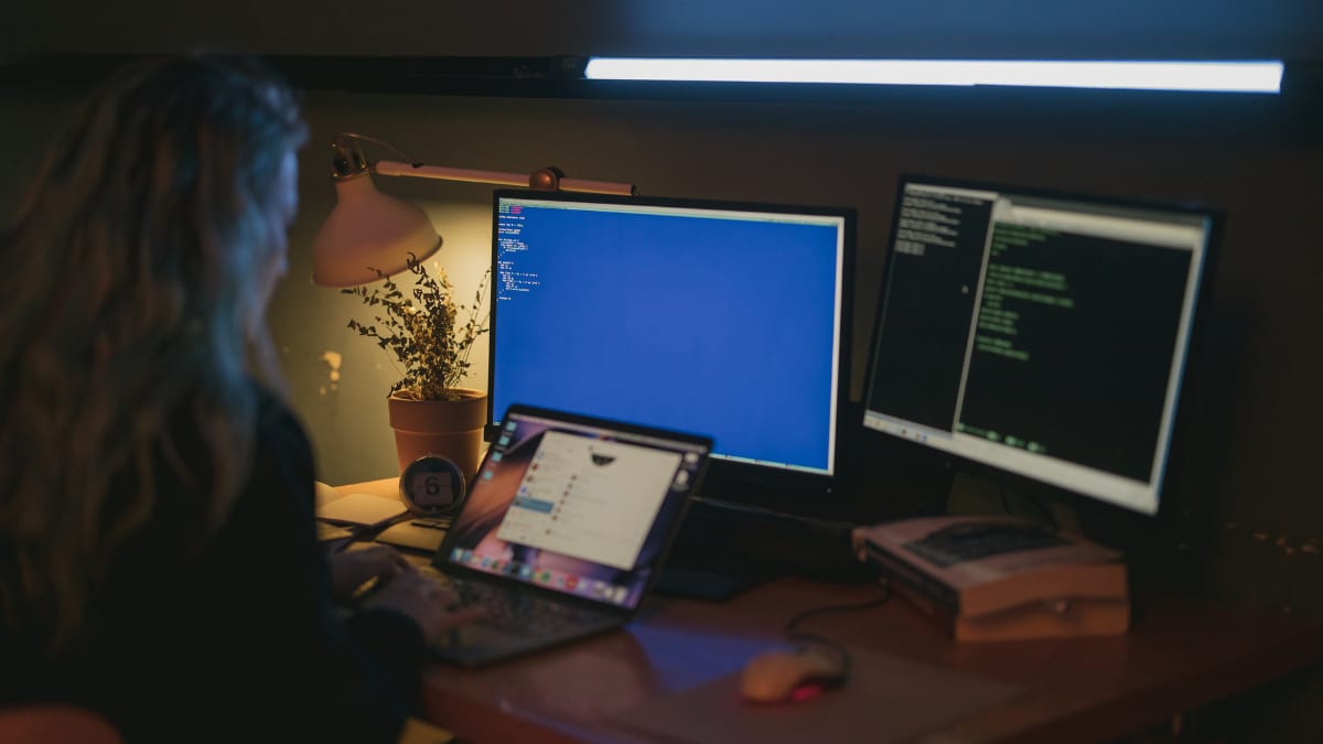 someone sitting at a desk in front of three computers