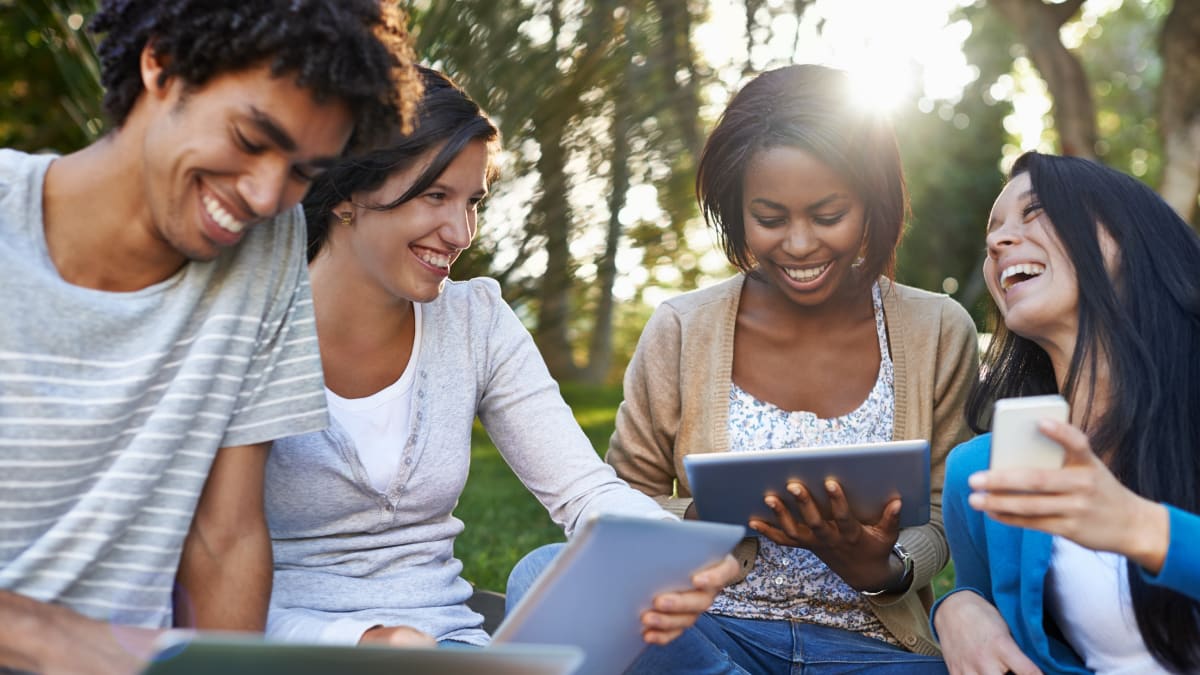 college students sitting outside together using various electronic devices