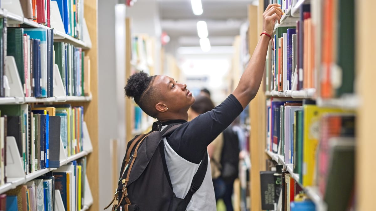 college student pulling a book from the shelves in the library