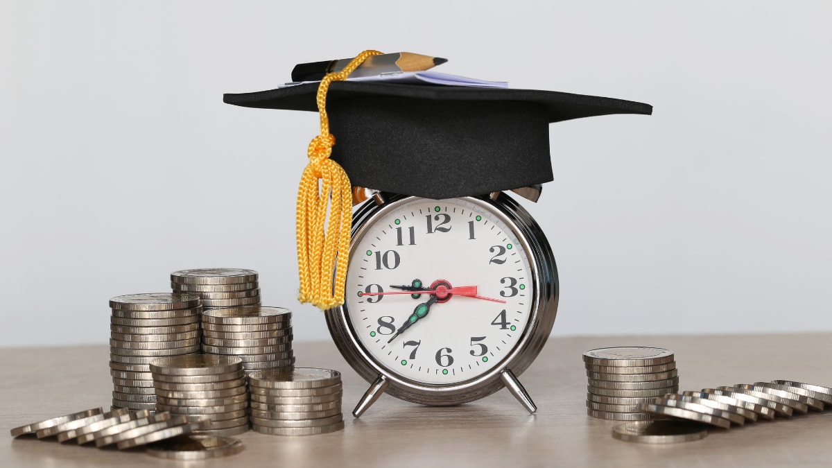 alarm clock with a graduation cap sitting on top and coins stacked around it