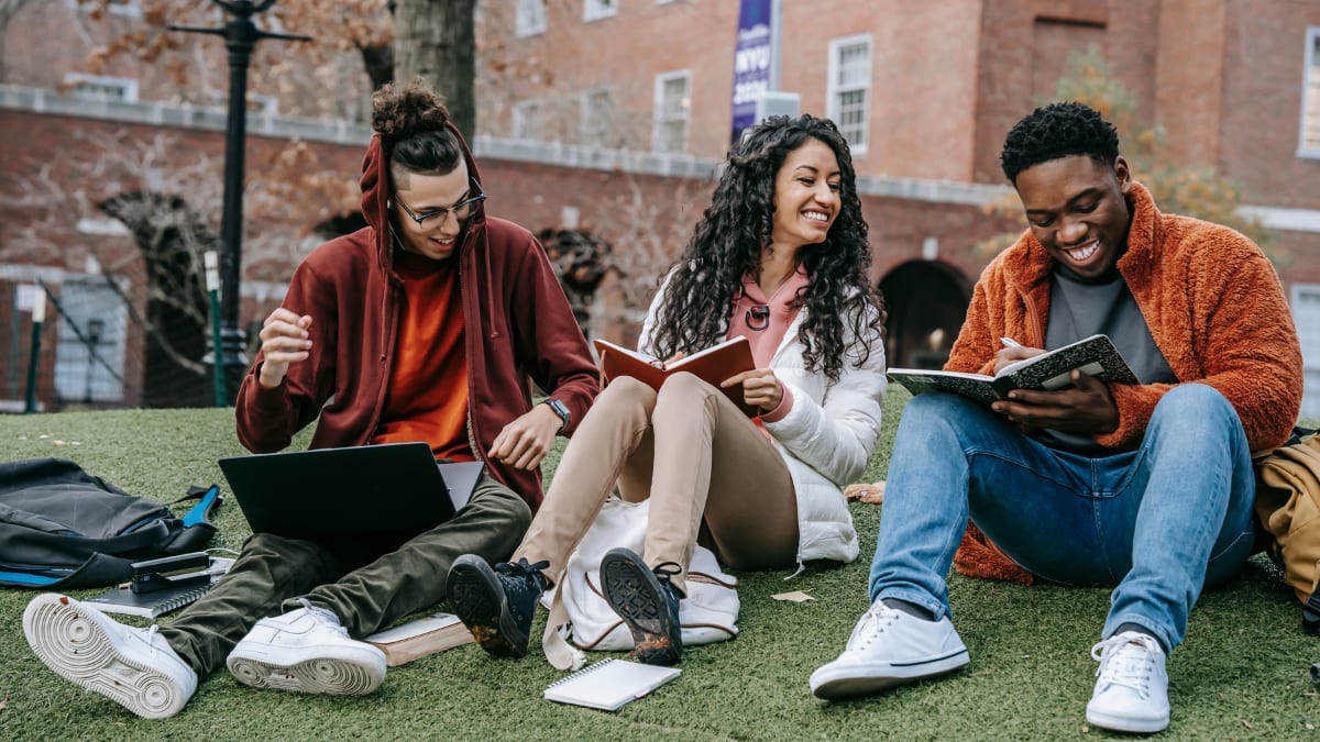 three students sitting together outside on a college campus