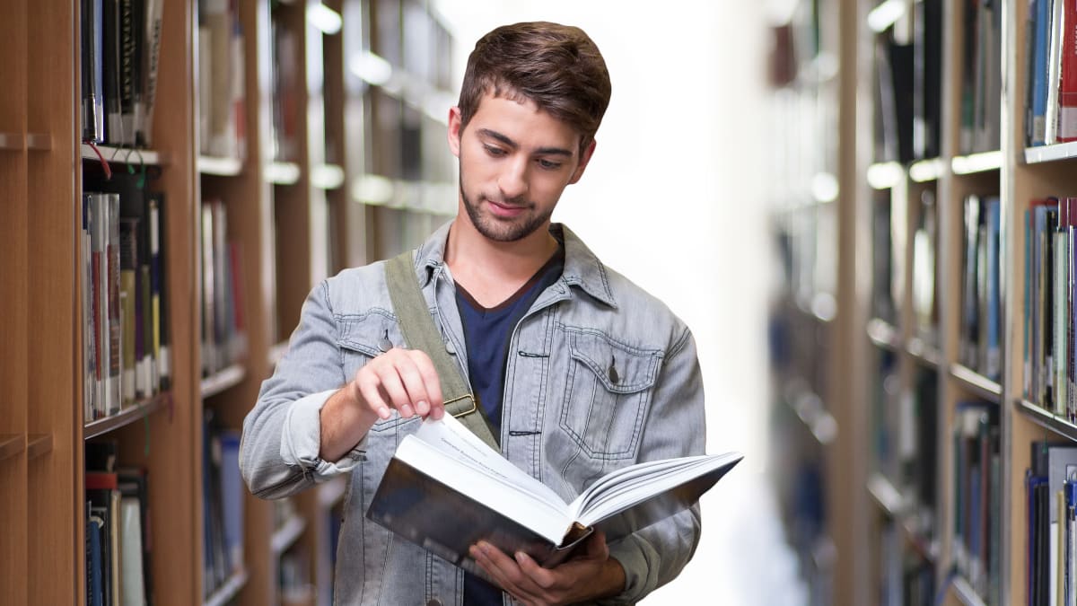 college student looking at a book in the library