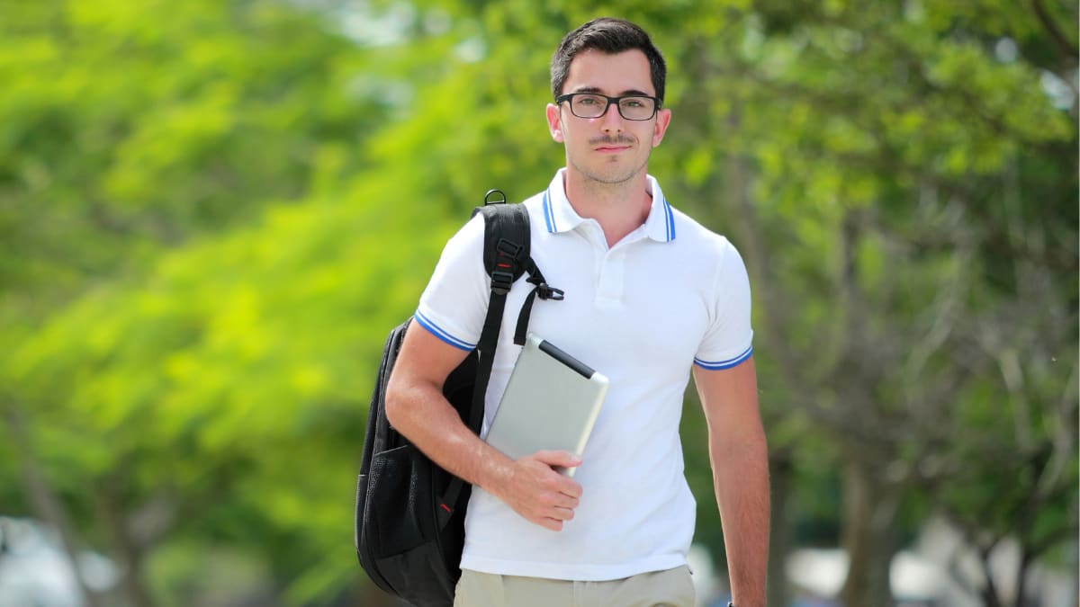 online college student walking outside carrying a tablet