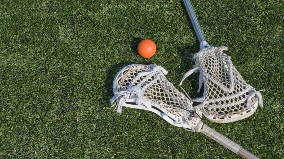 two lacrosse sticks and a ball laying in the grass