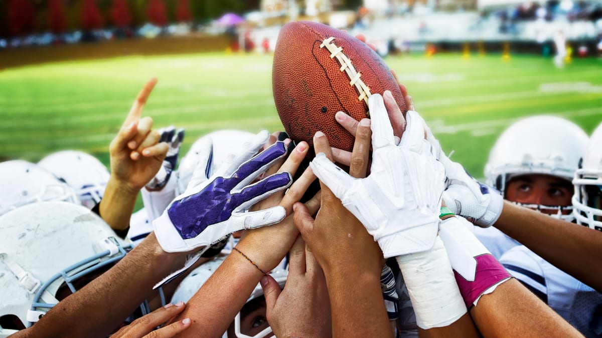 team of football players all touching a football that is being held up by a player
