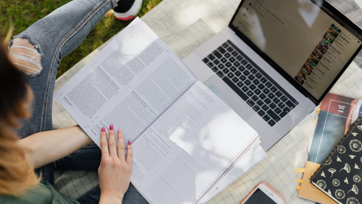 college student sitting outside with a computer and textbook