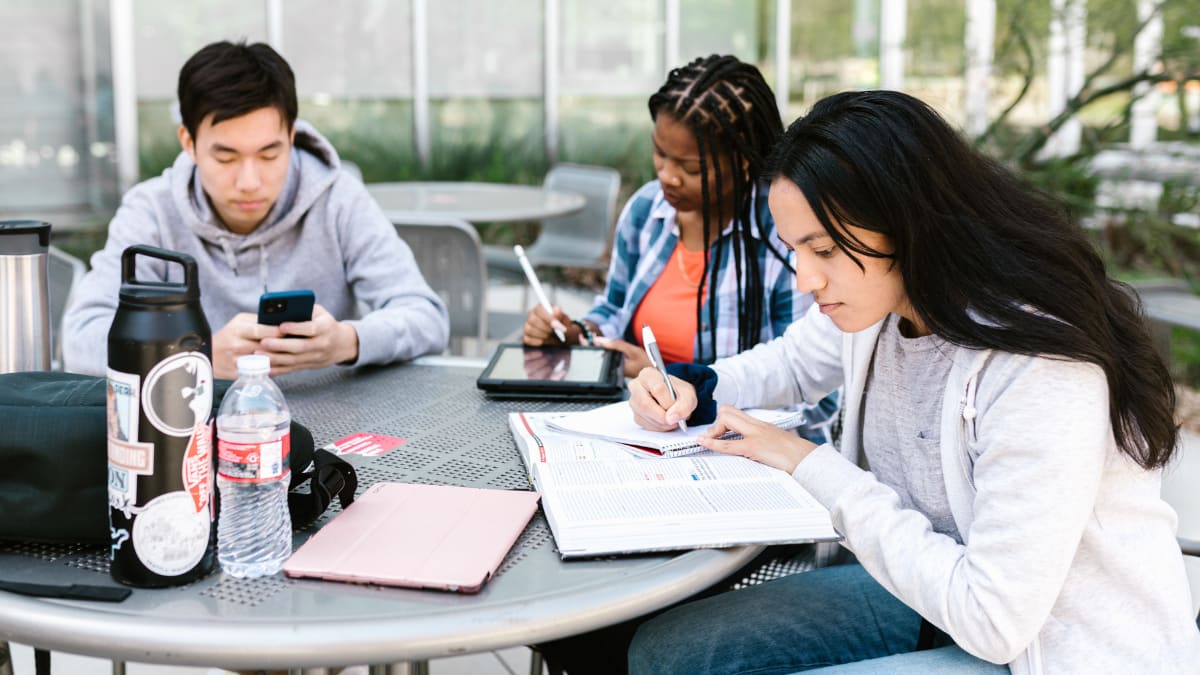 three students sit together outside at a college campus