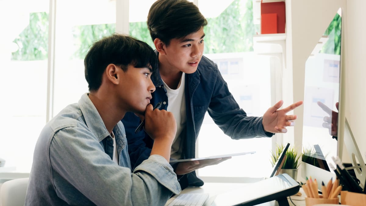 two cyber security students looking at a computer screen discussing something